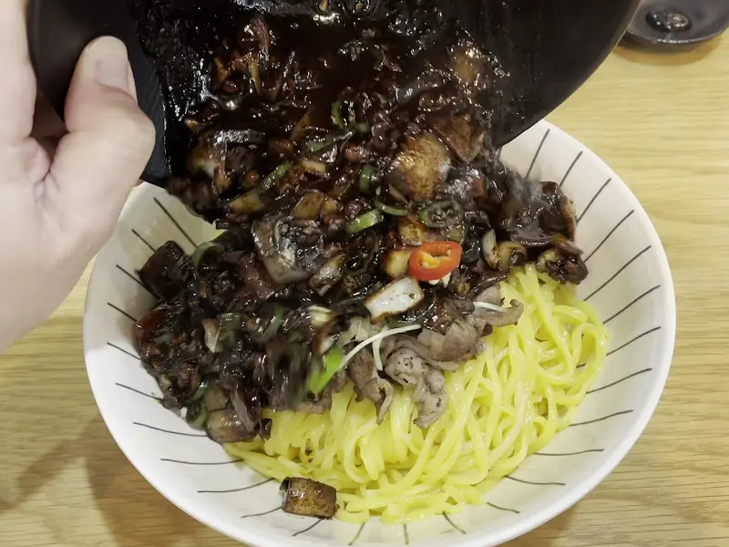 갓 볶은 짜장 소스를 면 위에 부어 먹음직스러운 짜장면을 만드는 모습