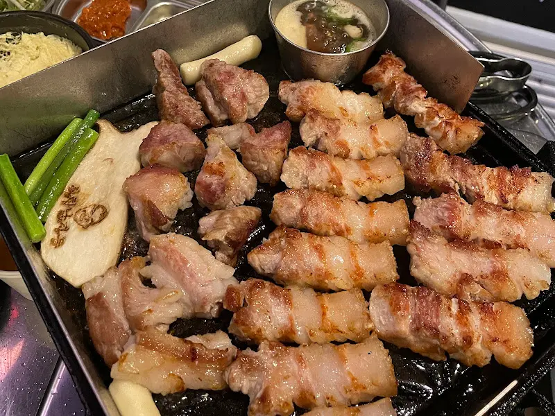 불판 위에 가지런히 놓인 오겹살과 버섯, 떡