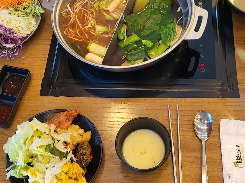 테이블 위에 놓인 샤브샤브 냄비와 다양한 채소, 소스, 월남쌈 재료들