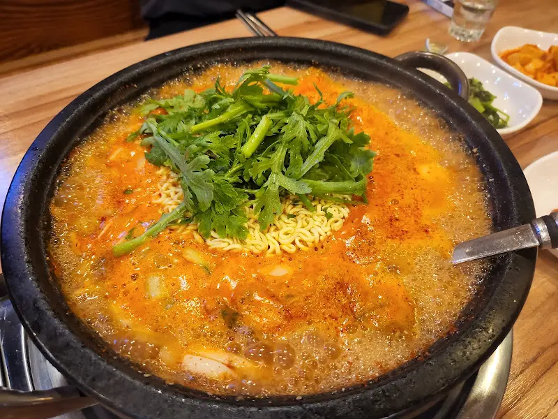 냉이가 듬뿍 올려진 채 끓고 있는 부대찌개의 클로즈업 샷