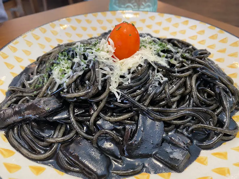 검은 면 위에 치즈와 토마토가 올라간 오징어 먹물 파스타