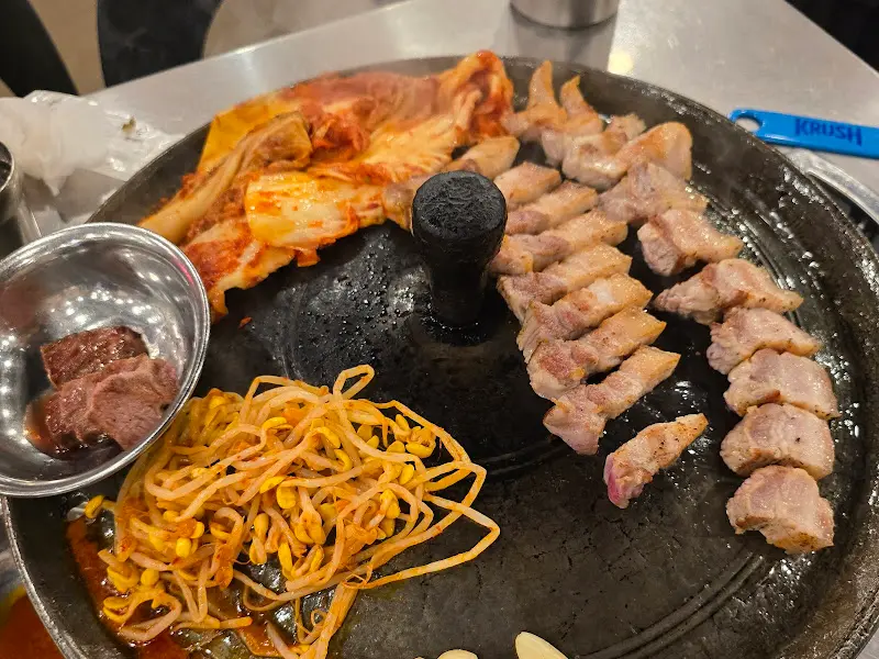 솥뚜껑에 구워진 삼겹살과 김치, 콩나물