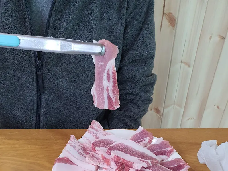 잘 구워진 삼겹살을 집게로 드는 모습