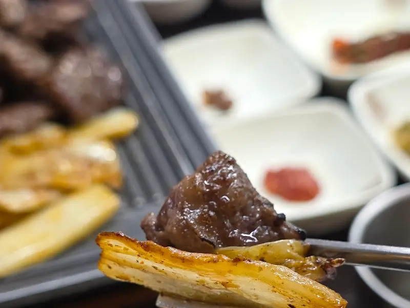 잘 익은 고기를 젓가락으로 집어올려 김치와 함께 먹으려는 모습