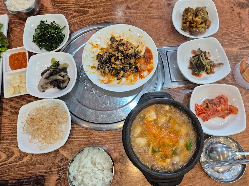 우렁쌈장과 곁들임 반찬들, 그리고 따뜻한 된장찌개가 놓인 테이블