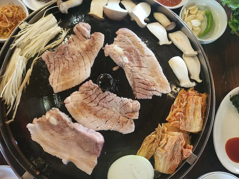 솥뚜껑에 구워지는 삼겹살과 김치, 버섯