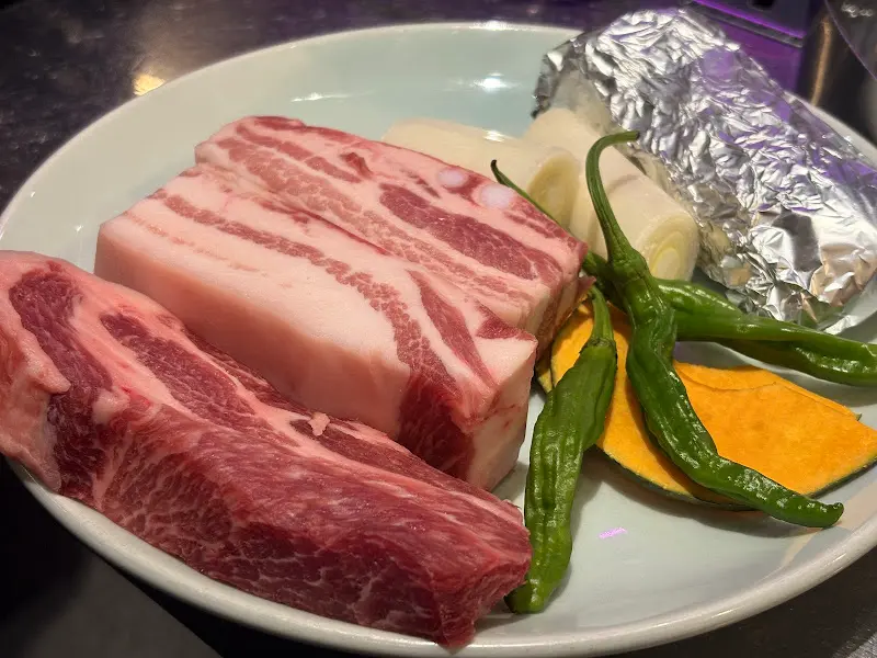 두툼한 숙성 삼겹살과 곁들임 채소가 담긴 접시