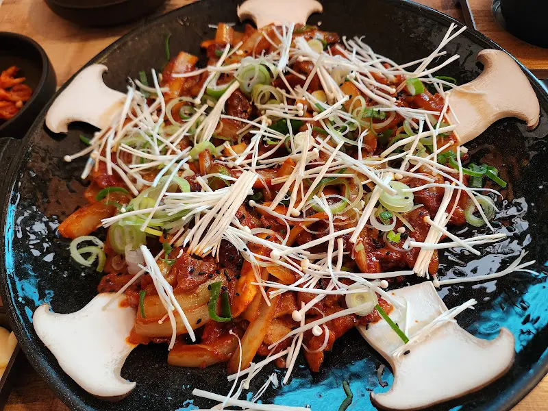 제육철판볶음 위에 팽이버섯과 파가 듬뿍 올려져 있는 모습