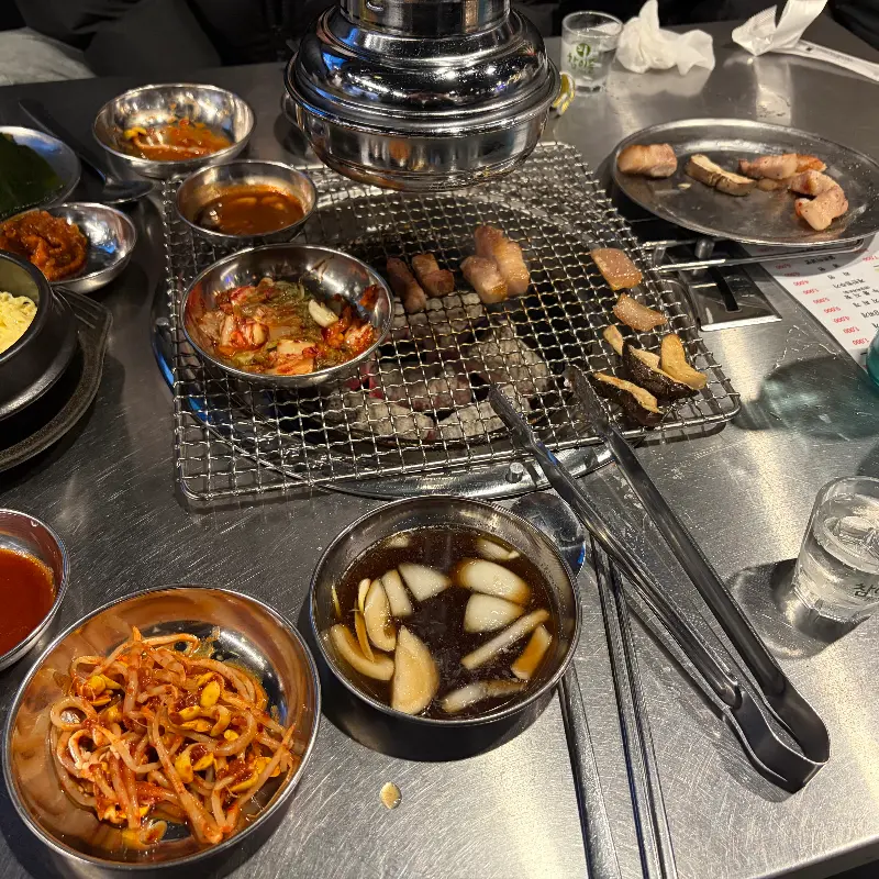 불판 위에 삼겹살, 김치, 콩나물 무침이 함께 구워지고 있다.