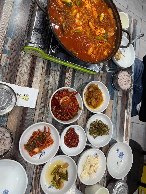 밑반찬이 푸짐하게 차려진 테이블 위에 갈치조림 냄비가 놓여 있다.