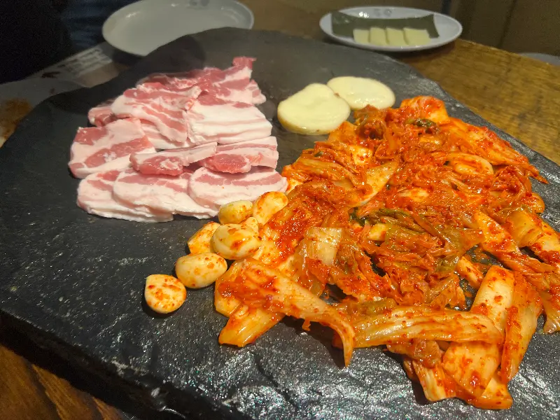 돌판 위에 고기, 김치, 마늘이 함께 구워지고 있는 모습
