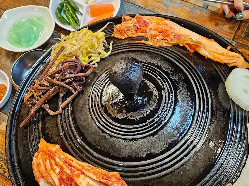 솥뚜껑 위에 김치, 콩나물, 고사리가 함께 구워지는 모습