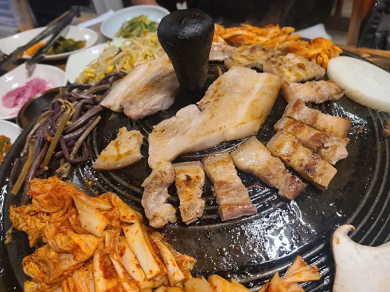 솥뚜껑 위에 삼겹살과 다양한 밑반찬이 올려져 있는 전체적인 모습