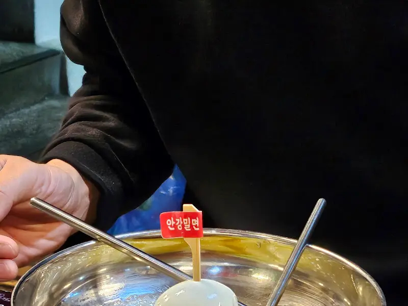 밀면 위에 얹어진 계란 고명과 '안김밀면'이라고 적힌 깃발