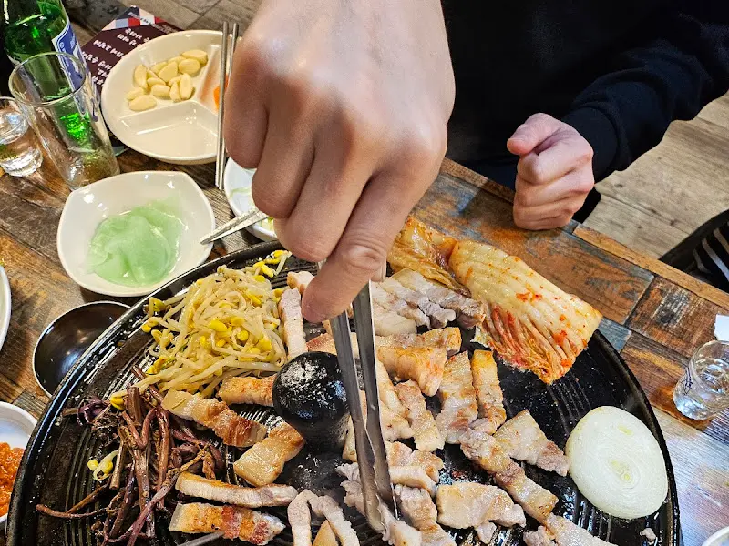 솥뚜껑 위에 구워진 삼겹살을 젓가락으로 집는 모습