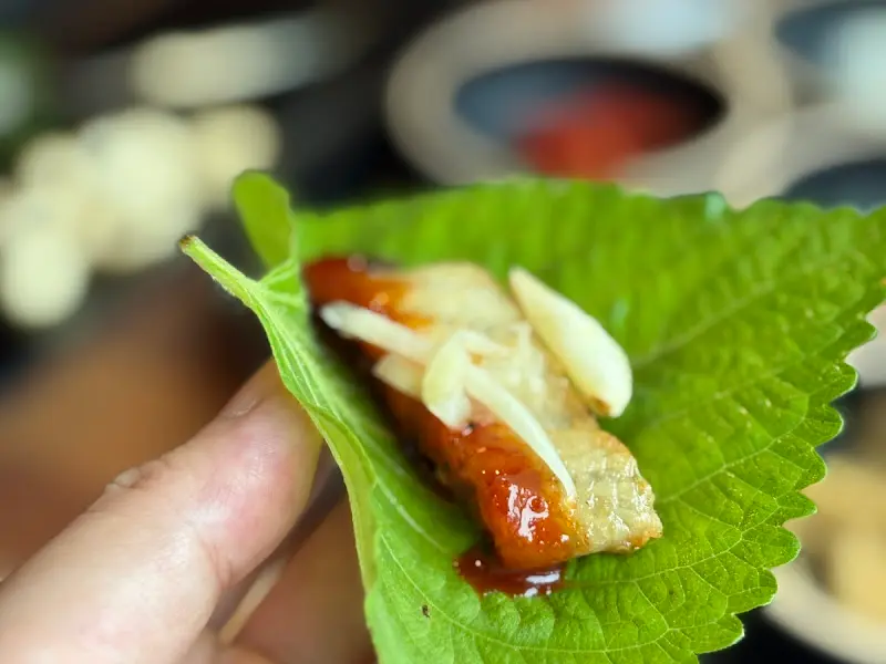 깻잎 위에 장어, 생강, 소스를 올려 한입에 먹기 좋게 쌈을 싼 모습