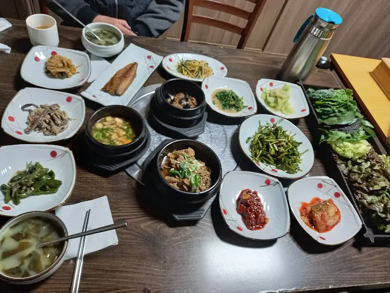 다채로운 밑반찬과 우렁쌈밥, 고추장 양념이 먹음직스럽게 담겨 있는 모습