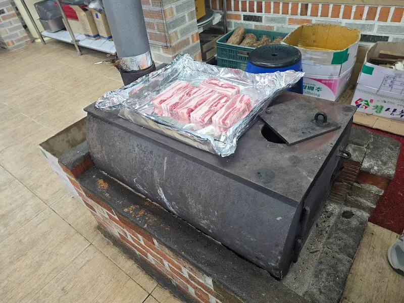 장작 화로 위에 올려진 삼겹살. 두툼한 고기에서 윤기가 흐른다.