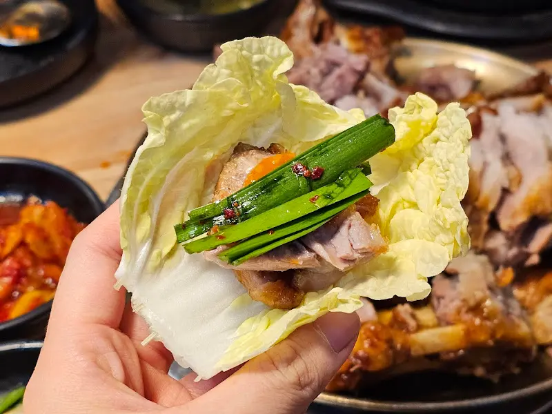 잘 차려진 밑반찬과 족발을 손으로 쌈을 싼 모습