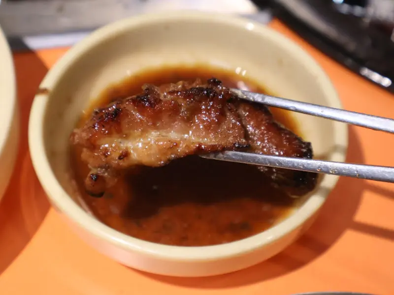 윤기가 흐르는 돼지갈비 한 점을 젓가락으로 집어 양념에 찍어먹는 모습