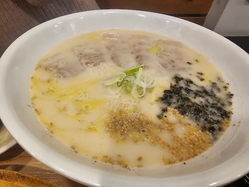 사골 고기국수의 클로즈업 사진. 하얀 국물과 고기, 김가루, 깨가 보인다.