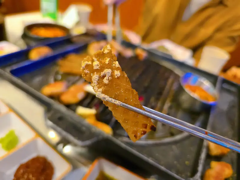 맛있게 구워진 돼지 껍데기를 집게로 들어올리는 모습