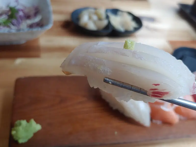 젓가락으로 흰살 생선 초밥을 집어 올리는 모습