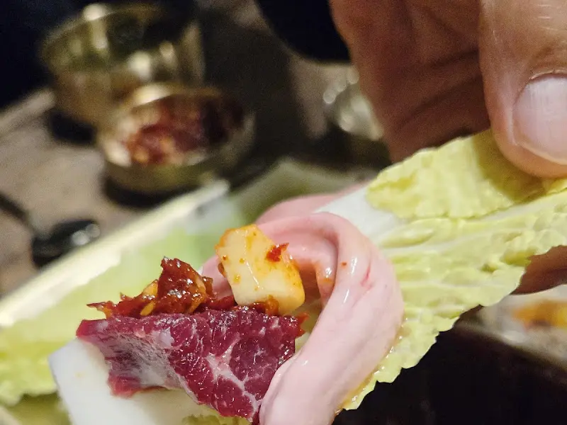 배추에 뭉티기, 간, 양념장을 싸서 먹는 모습