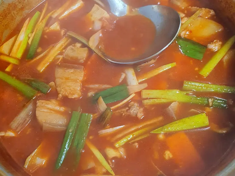 국자로 고추장찌개를 뜨는 모습, 돼지고기와 파가 보인다.