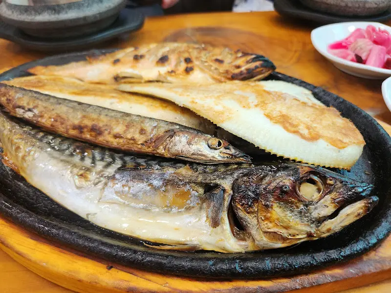 윤기가 흐르는 고등어구이, 가자미구이, 열기구이가 무쇠판에 담겨져 있는 모습