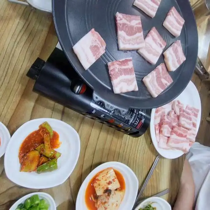 불판 위에 올려진 삼겹살과 다양한 반찬들