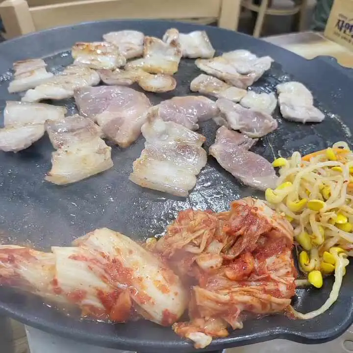 불판 위에 구워진 삼겹살과 김치, 콩나물