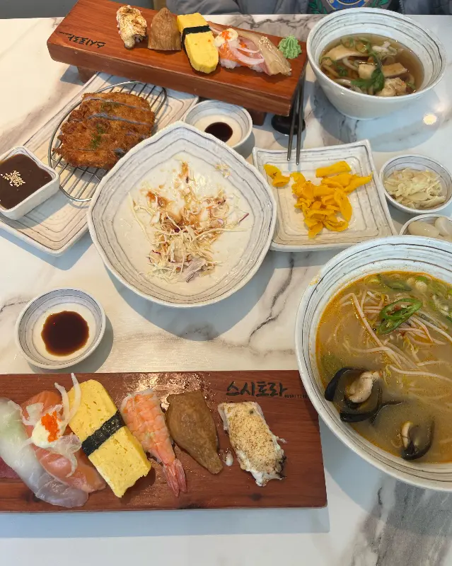 테이블 위에 놓인 초밥, 돈까스, 우동 등의 다양한 음식