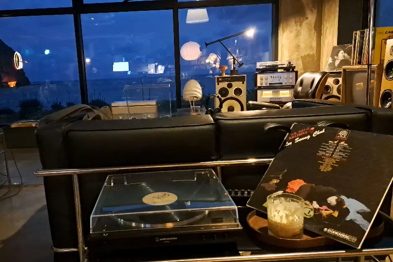 LP 턴테이블과 음료가 놓인 테이블, 뒤로 보이는 바다 풍경이 인상적이다.