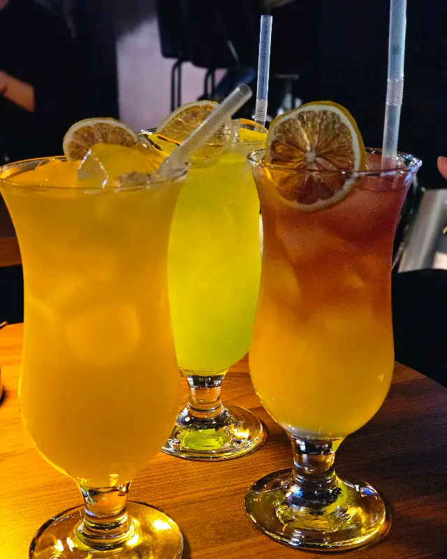 다채로운 색감의 칵테일 세 잔이 나란히 놓여 있다. 잔 위에는 말린 오렌지 조각이 장식되어 있다.