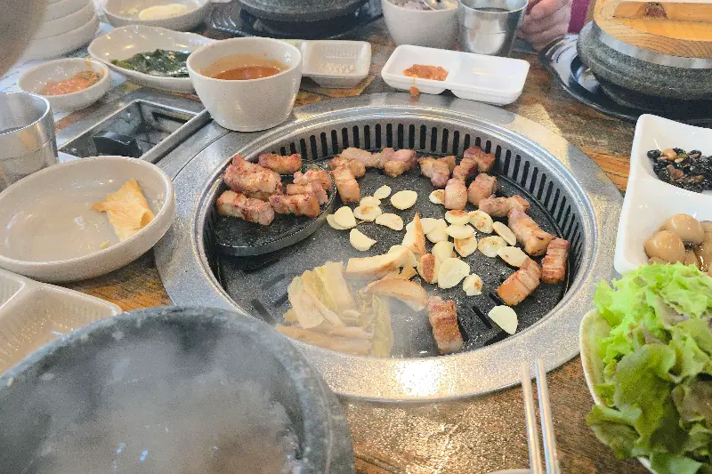 솥뚜껑 위에서 익어가는 삼겹살과 마늘