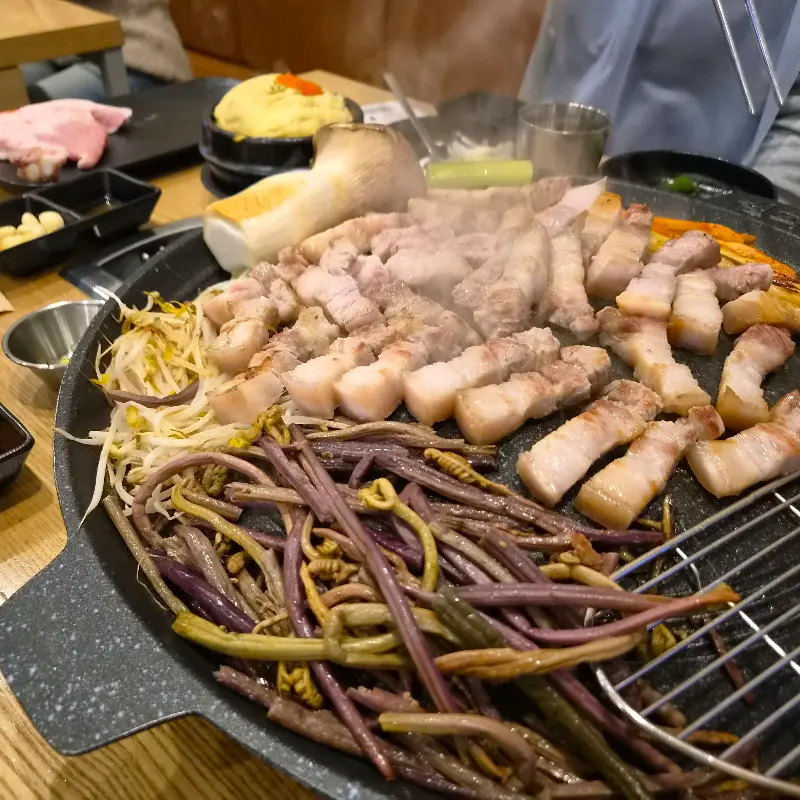 잘 구워진 삼겹살이 솥뚜껑 위에 가득 쌓여있는 모습