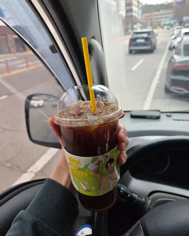 차 안에서 아이스 아메리카노를 들고 있는 모습