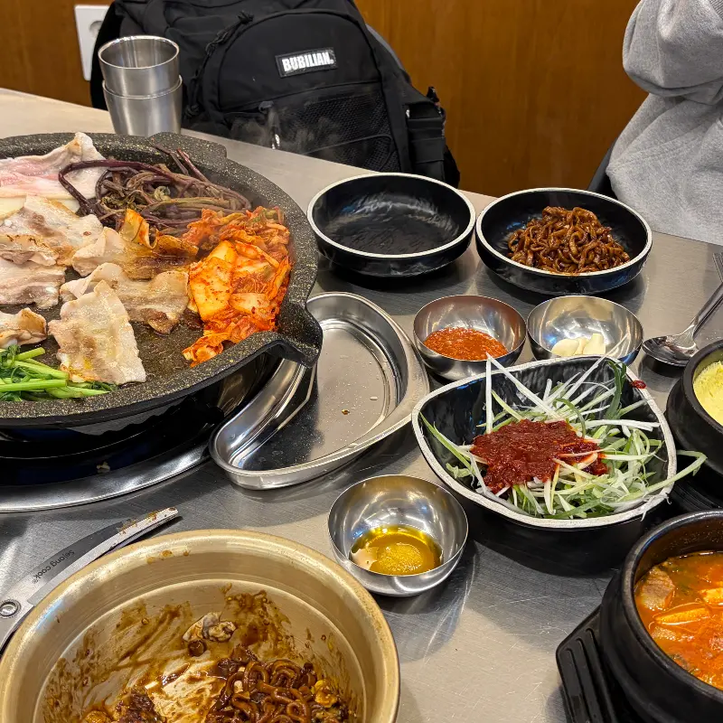 테이블 위에 푸짐하게 차려진 냉동 삼겹살과 다양한 반찬들