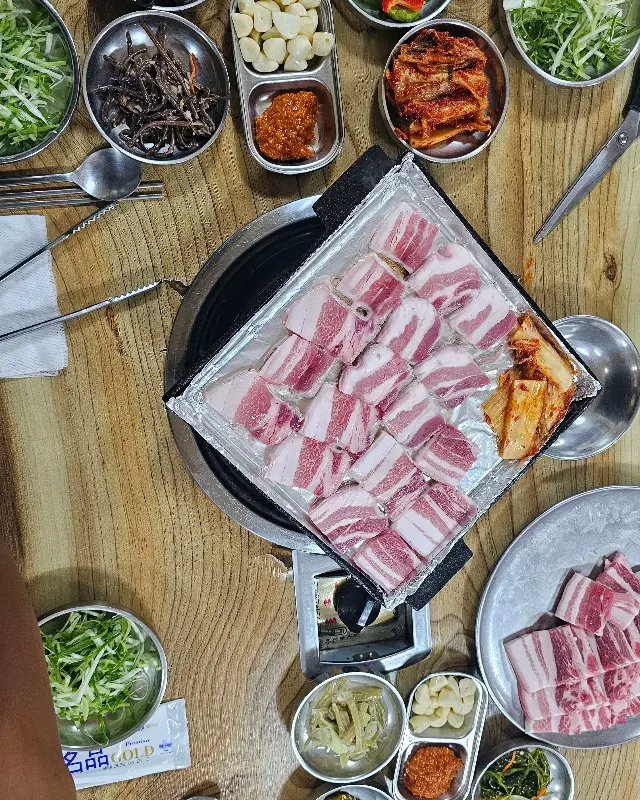 불판 위에 가지런히 놓인 삼겹살, 김치와 마늘이 함께 구워져 풍미를 더한다.