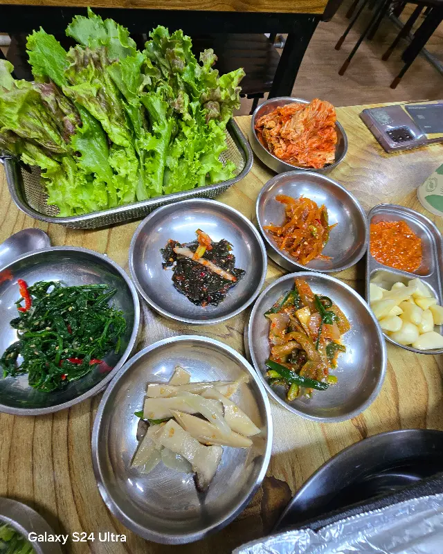 싱싱한 쌈 채소와 다채로운 밑반찬, 콩나물무침, 깻잎 장아찌 등 푸짐한 구성이 인상적이다.