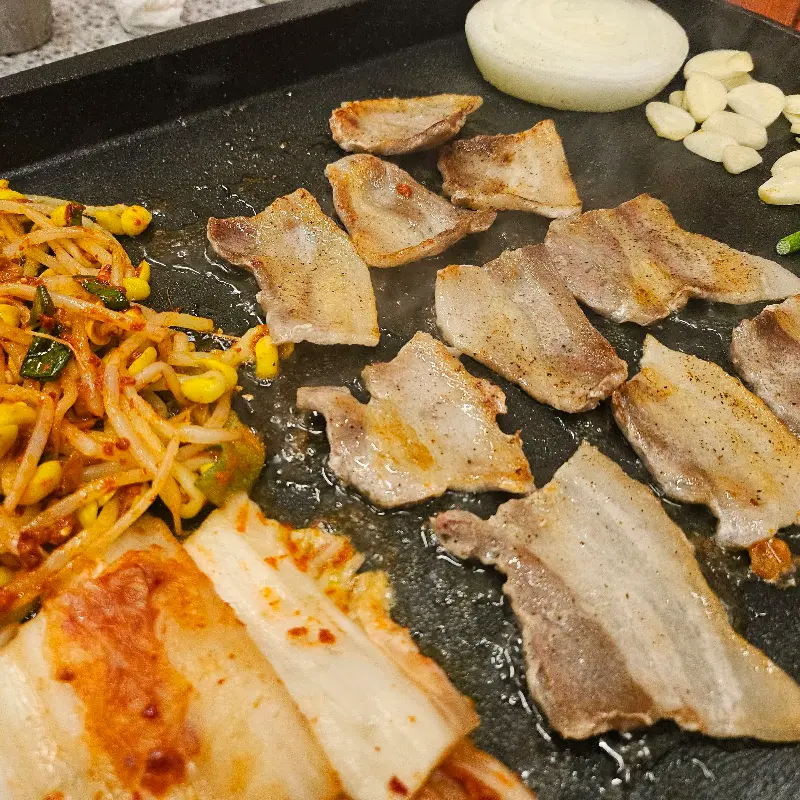 불판 위에서 익어가는 삼겹살과 김치, 콩나물