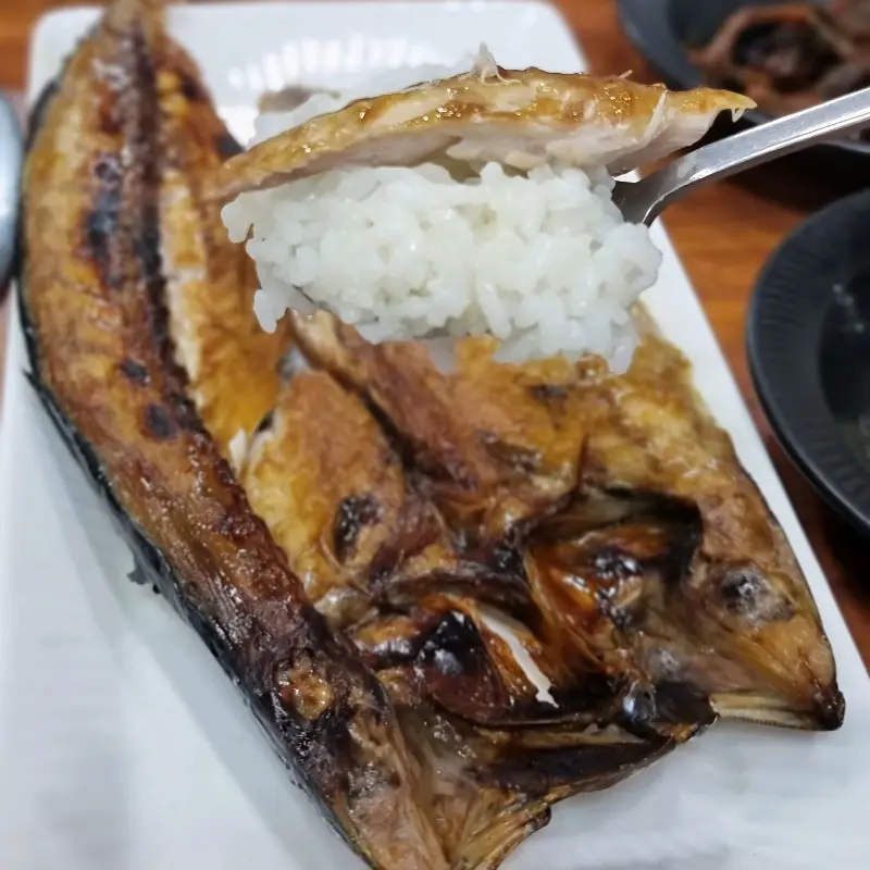 윤기가 흐르는 고등어 구이 한 점을 밥 위에 올려 먹는 모습