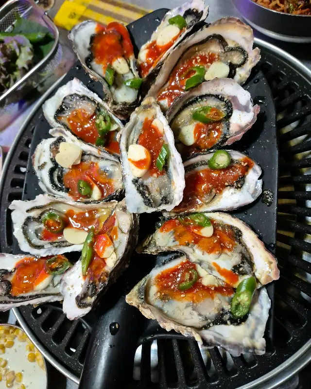 싱싱한 석화에 초장, 마늘, 고추를 곁들여 먹는 모습