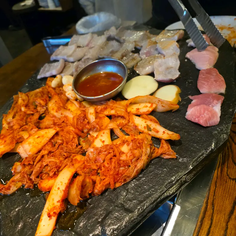 돌판 위에 가득찬 천겹살, 김치, 감자, 마늘