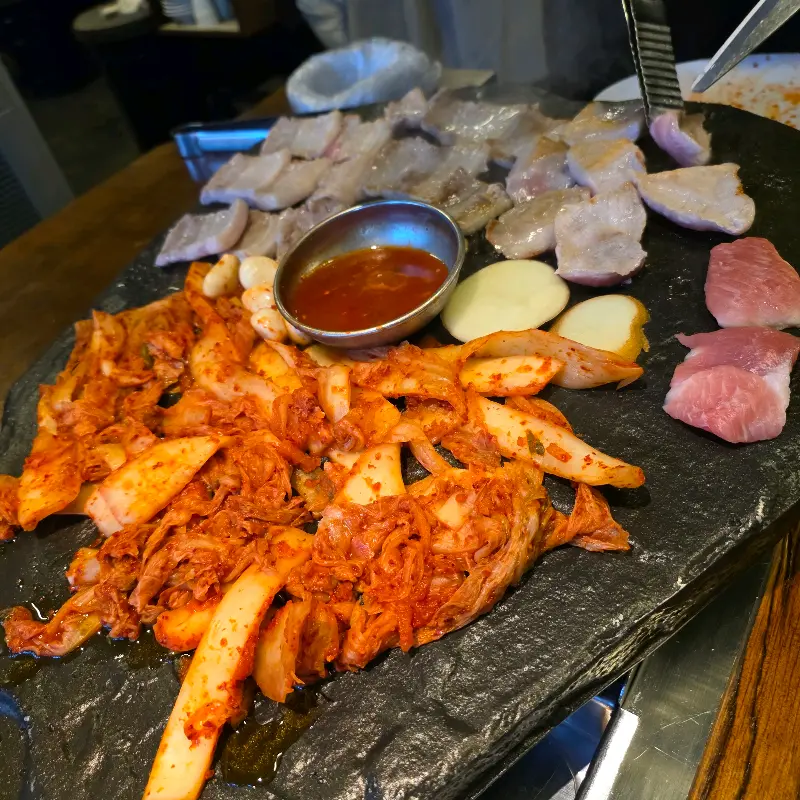 돌판 위에 구워지는 천겹살, 김치, 감자, 마늘