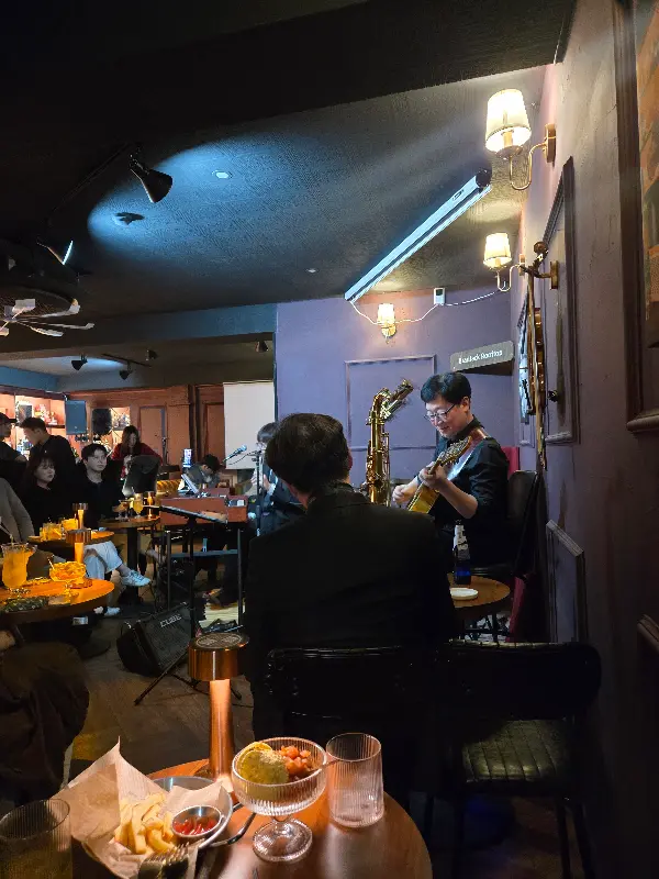 어두운 분위기 속에서 재즈 공연이 펼쳐지고 있고, 테이블에는 칵테일과 안주가 놓여 있다.