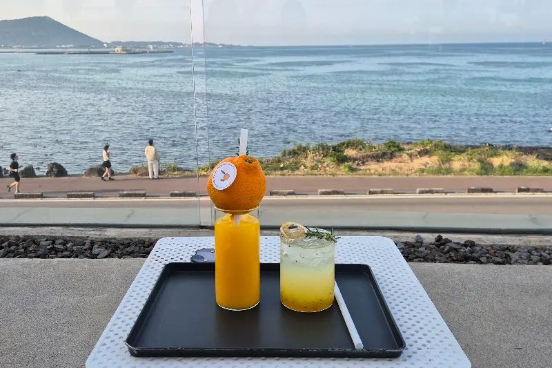 한라봉 쥬스와 다른 음료가 놓인 테이블, 뒤로 보이는 제주 바다