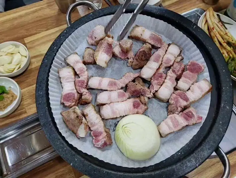돌판 가득 삼겹살이 담겨져 있고, 가운데 양파가 놓여져 있다.