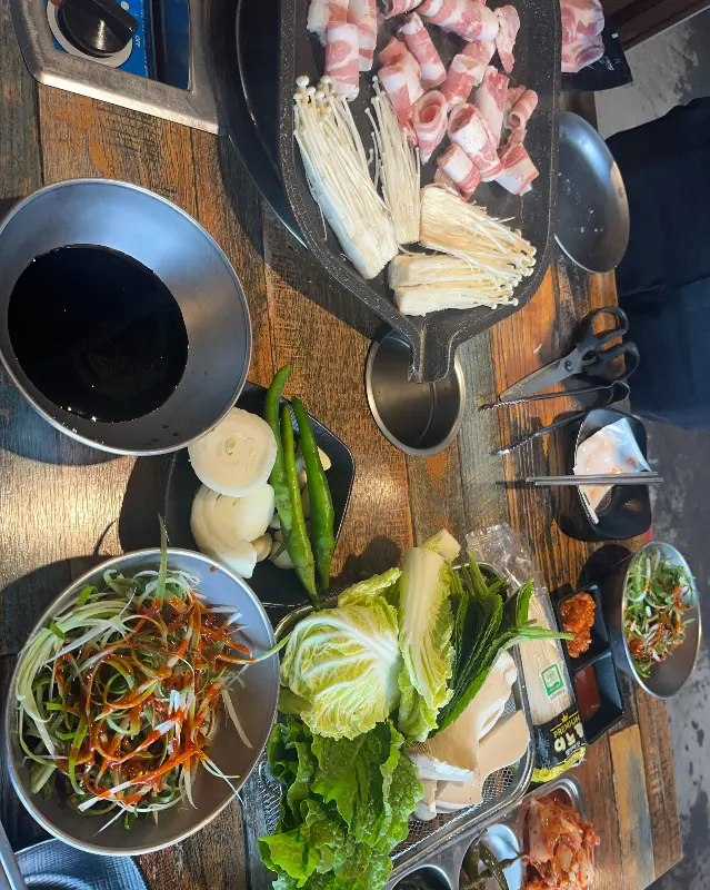 불판 위에 가지런히 놓인 신선한 삼겹살과 버섯